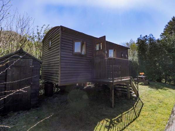A wooden cabin with a deck and a small porch, surrounded by trees.