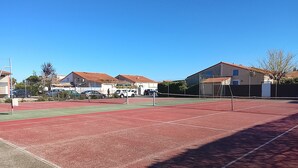 Una pista de tennis amb una xarxa, envoltada d'edificis amb teulades vermelles.