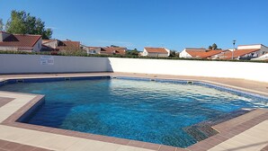 Una piscina d'aigua cristal·lina blava, envoltada per un solarium amb rajoles i una paret blanca.