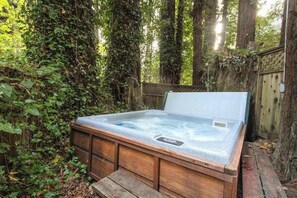 Een hottub in een bebost gebied, met een houten terras en een houten omheining.
