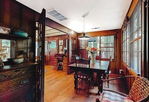 A wooden dining room with a table and chairs, a hanging light fixture, and a view through large windows. - Guerneville Clearheart Grove: Dog-Friendly Redwood Cabin (Guerneville)