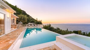 Ein Pool mit Meerblick, eine Terrassenfläche mit Sitzgelegenheiten und eine Steinmauer.