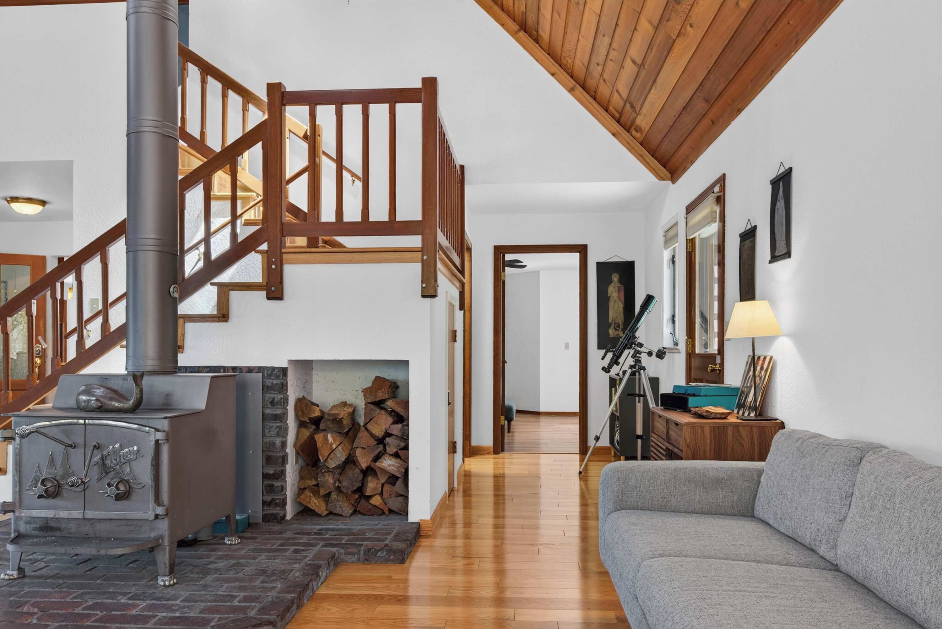 A living room with a fireplace, a sofa, a wooden staircase, and a ceiling with exposed beams.