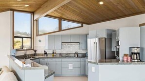A modern kitchen with grey cabinets, stainless steel appliances, and a wooden ceiling. - Architect-Designed Bodega Bay Home w/ Ocean Views & Hot Tub - 2 King Suites (Bodega Bay)