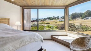 A bedroom with a large bed, a wicker chair, and a view of a landscape through a large window. - Architect-Designed Bodega Bay Home w/ Ocean Views & Hot Tub - 2 King Suites (Bodega Bay)