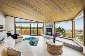 A spacious living area with a fireplace, large windows, and a view of greenery. - Architect-Designed Bodega Bay Home w/ Ocean Views & Hot Tub - 2 King Suites (Bodega Bay)