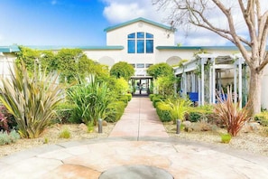 A building with a central entrance, surrounded by a garden with various plants and a pathway leading to the entrance. - Napa 2BR Silverado condo — two king suites, golf views & pool (Napa)