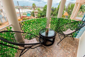 A balcony with two black metal chairs, a glass table, and a view of a residential area. - Modern Cozy 2 bedroom Retreat with Private balcony (Kampala)