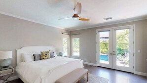 Une chambre à coucher comprenant un lit, un banc, un ventilateur de plafond et de grandes portes-fenêtres coulissantes.
