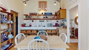 Una cucina con un tavolo e sedie in legno, uno schienale piastrellato bianco e cartelli che indicano 'Grilled Fish' e 'Fresh Oysters'.