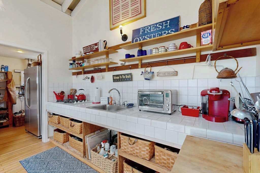 A kitchen with white tiles, a stainless steel refrigerator, a toaster, and a coffee maker.