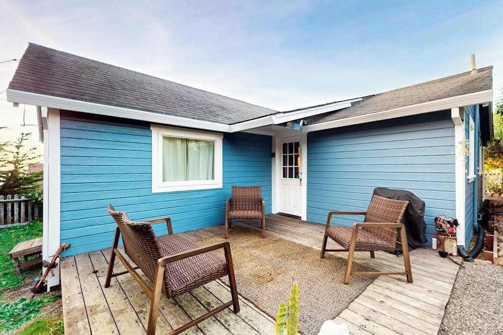 Una casa con facciata blu, un portico coperto con mobili in vimini e un'auto in garage.