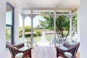 A covered porch with wicker furniture and a view of a garden.