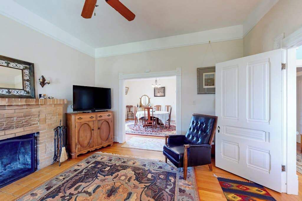 A living room with a fireplace, a television, a large rug, a dining area with a table and chairs, and a door.