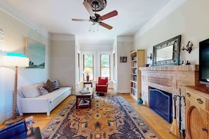 A living room with a sofa, a coffee table, a fireplace, a bookshelf, and a ceiling fan.