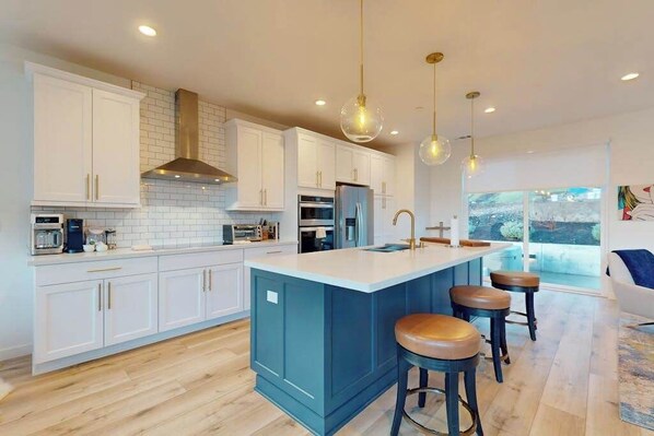 A modern kitchen with white cabinets, a blue island, and pendant lighting.