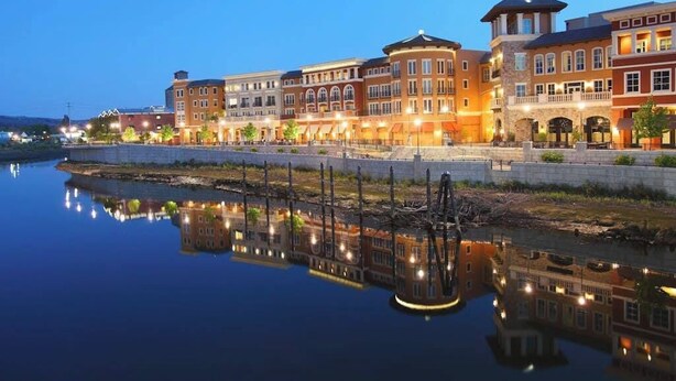 Un hôtel situé au bord de l’eau, composé de plusieurs bâtiments, dont le reflet se mire dans l’eau, et un pont reliant les différentes structures.
