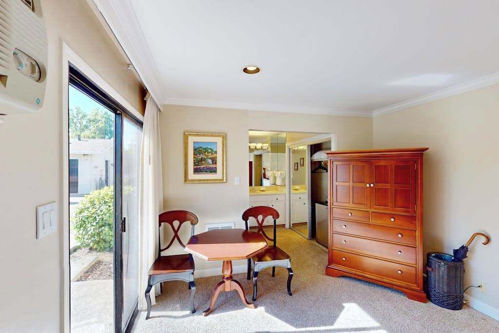 A room with a dining table, two chairs, a wooden cabinet, and a sliding glass door leading outside.