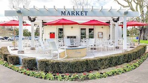 Un marché avec des tables à l’extérieur, un foyer et des parasols rouges.
