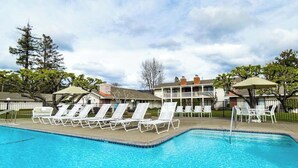 Une piscine entourée de bâtiments et d’arbres, avec des chaises longues et des parasols.