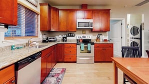 A kitchen with wooden cabinets, a microwave, an oven, a dishwasher, and a dining area with a table.