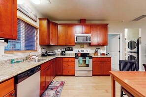A kitchen with wooden cabinets, a microwave, an oven, a dishwasher, and a dining area with a table.