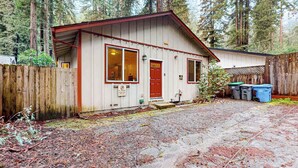 A single-story cabin with a red door and windows, surrounded by a wooden fence and trees.