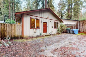 A single-story cabin with a red door and windows, surrounded by a wooden fence and trees.