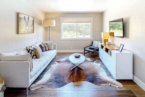A modern living room with a white sofa, a round coffee table, a leather rug, a side table, and a TV mounted on the wall.