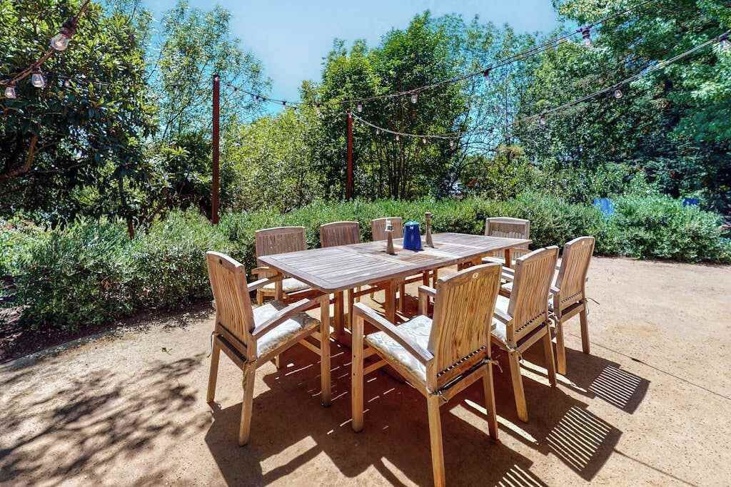 Conjunto de mesa e cadeiras de madeira ao ar livre num jardim com luzes de corda.