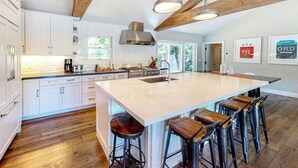 Uma cozinha moderna com armários brancos, uma ilha grande com banquetas e um lustre.