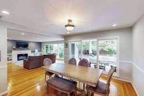 A spacious dining area with a wooden table and chairs, a fireplace, and a view of the outdoors through large windows. - Santa Rosa Renovated Home with Fireplace & Private Patio (Santa Rosa)