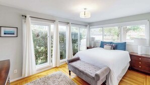 A bedroom with a bed, a nightstand, a lamp, and a view through large windows. - Renovated Wine Country Ranch w/ Private Patio & AC - Sleeps 4 in Santa Rosa (Santa Rosa)