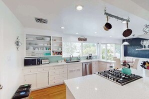 A modern kitchen with white cabinetry, a central island, a stove, and a window with a view. - Santa Rosa Renovated Home with Fireplace & Private Patio (Santa Rosa)