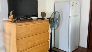A wooden dresser with a flat-screen TV, a fan, and a white refrigerator in a room with white walls and tiled flooring. - Peaceful Beautiful Countryside Perfect Destination (Tavira)