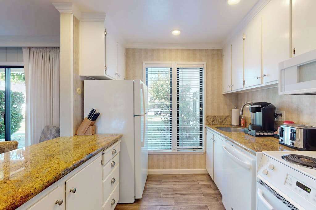 A modern kitchen with white cabinets, a granite countertop, a refrigerator, a coffee maker, and a toaster.