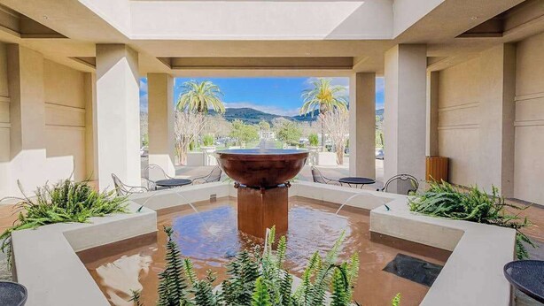 A covered outdoor area with a central water feature, seating, and views of palm trees and mountains. - Napa 2BR Silverado condo — two king suites, fireplace & pool (Napa)