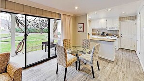 A modern kitchen with white cabinets, a glass dining table, and a view of a garden through large sliding glass doors. - Napa 2BR Silverado condo — two king suites, fireplace & pool (Napa)