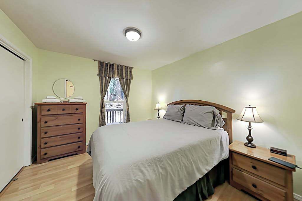 Een slaapkamer met een bed, een dressoir, een nachtkastje, een lamp en een raam met gordijnen.
