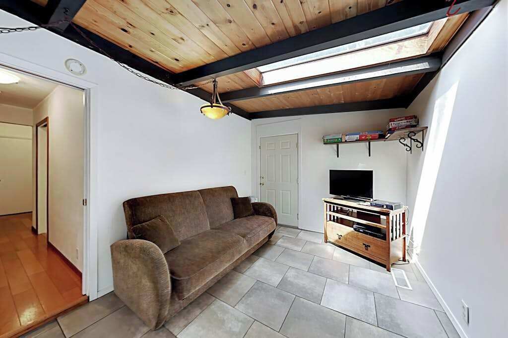 A room with a brown sofa, a wooden TV stand, and a ceiling with exposed beams.