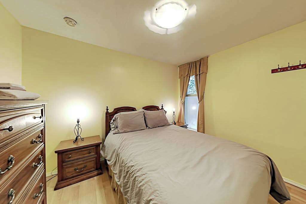 A bedroom with a bed, a dresser, a nightstand, and a wall-mounted light fixture.