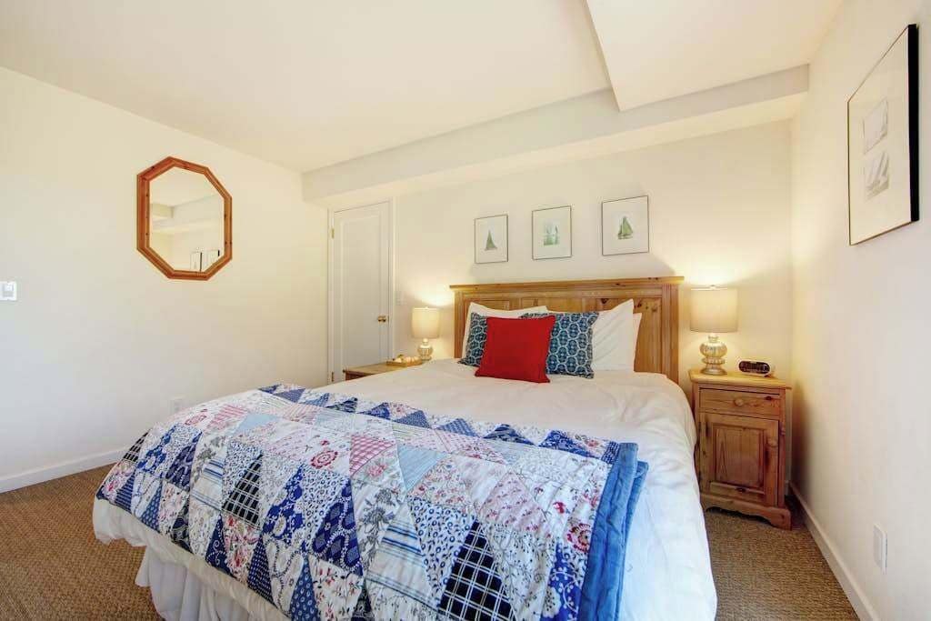 Ein Schlafzimmer mit einem großen Bett, einem Holz-Kopfstück, Nachttischlampen, einem Beistelltisch und einem Spiegel an der Wand.