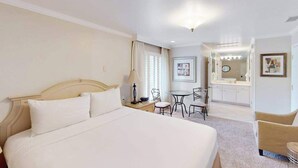 Habitación de hotel con una cama grande, un escritorio con una silla, una pequeña mesa con sillas, un espejo y un cuadro en la pared.