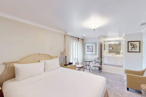 Een hotelkamer met een groot bed, een bureau met een stoel, een kleine tafel met stoelen, een spiegel en een lijst met een afbeelding aan de muur.