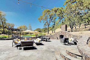 Un patio al aire libre con piso de piedra, sillones de descanso y una pérgola con sombrillas.