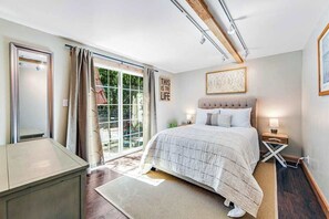 Quarto com cama, mesa de cabeceira e vista para o exterior.