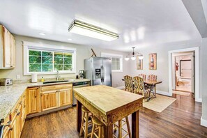 Uma cozinha com armários de madeira, uma ilha central e um espaço de jantar com cadeiras estampadas.
