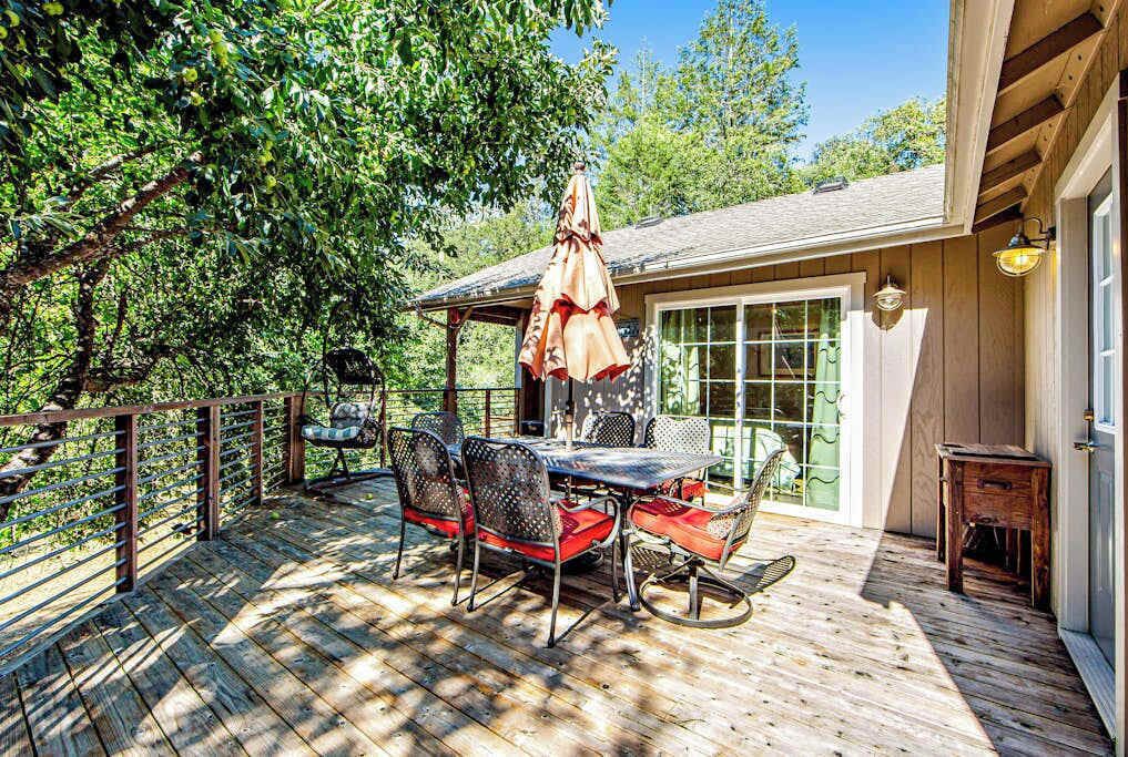A wooden deck with outdoor furniture, a covered seating area, and a view of the surrounding trees.