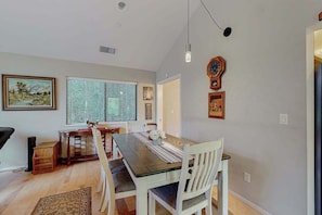 A dining area with a wooden table, white chairs, a window with blinds, a clock, and framed pictures on the wall. - Sebastopol Forest Retreat with Creek Trail (Sebastopol)