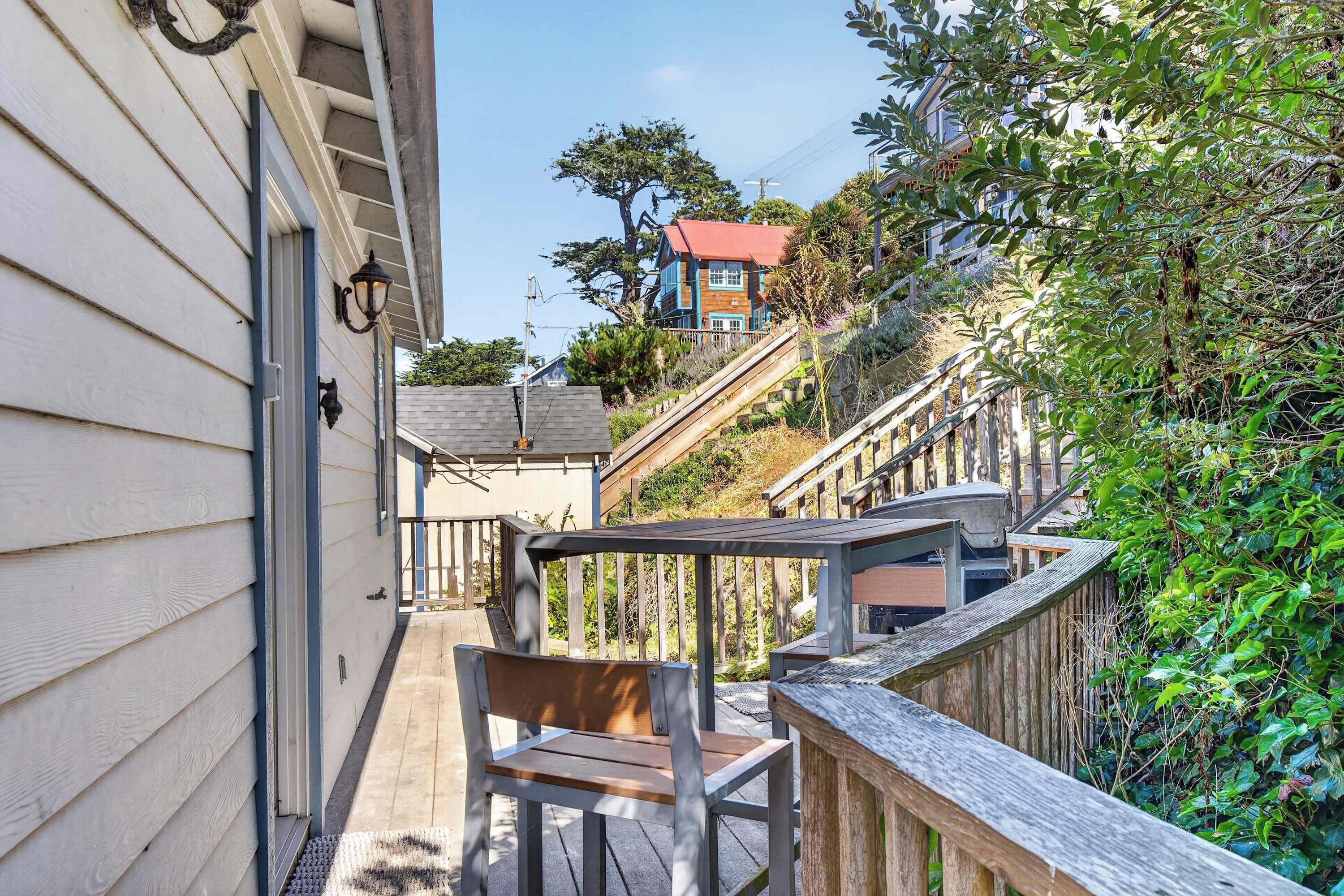 A wooden deck with a bench, a staircase leading to a house, and a view of a hill with trees.
